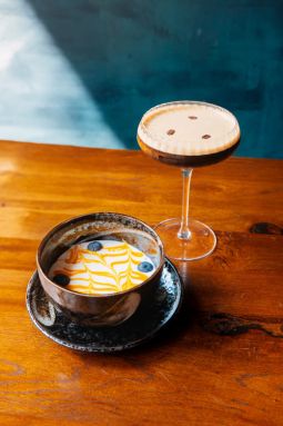 Leckerer Cocktail mit Dessert beim Amami Restaurant in Kiel auf gut beleuchtetem Holztisch vor türkisem Hintergrund